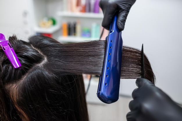 Friseur, der ein Haar begradigt, um das Haar zu begradigen Friseur, der an der Frisur einer Frau im Salon arbeitetHaarpflege Schöne, attraktive Frau in einem Schönheitssalon