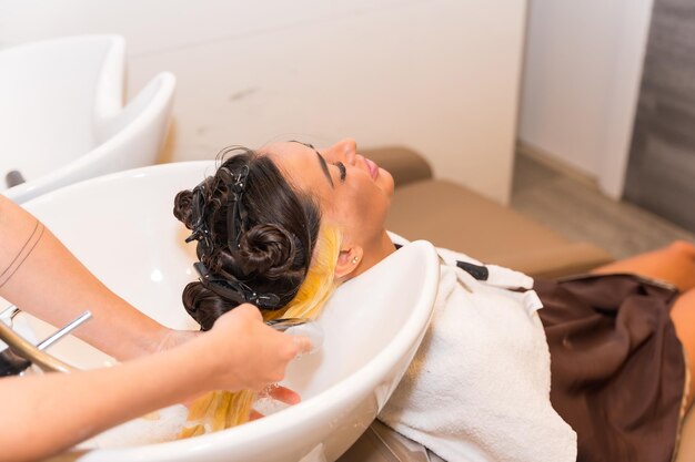 Friseur, der einer Kundin, die ihr Haar reinigt, einen blonden Farbstoff aufträgt