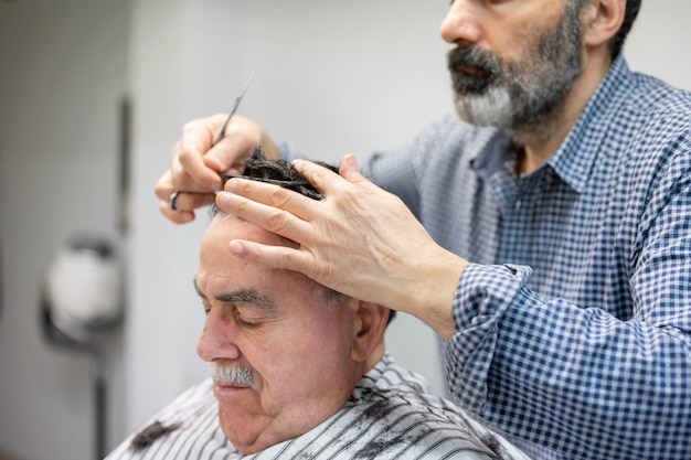 Friseur, der Haar des alten Mannes am Friseursalon trimmt.
