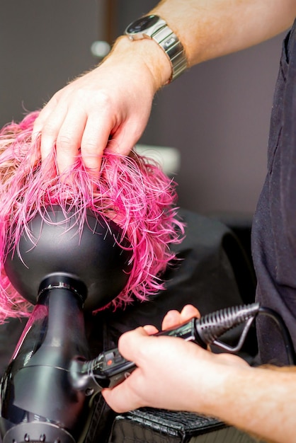 Friseur, der in einem Schönheitssalon eine Frisur mit einem Haartrockner auf nassem, rosafarbenem Haar macht.