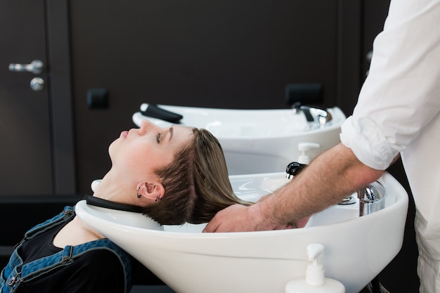 Friseur, der jugendlich Mädchenhaar im Schönheitssalon wäscht.