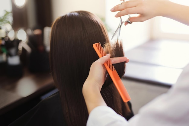 Friseur, der langes braunes Haar mit einer Schere im Schönheitssalon trimmt