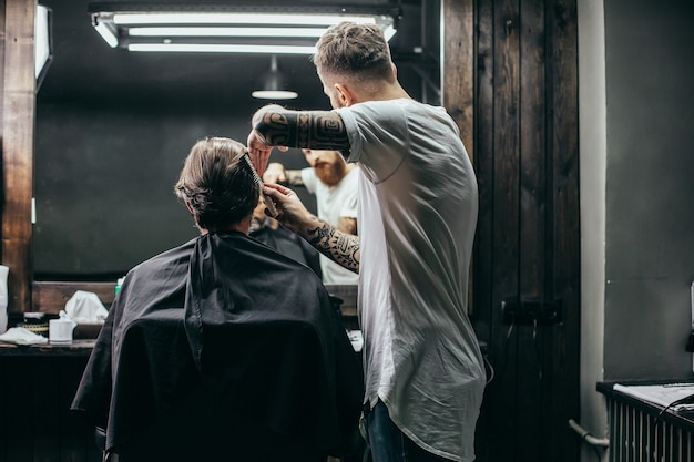 Friseur, der nahe an seinem Klienten steht und sein dunkles Haar kämmt