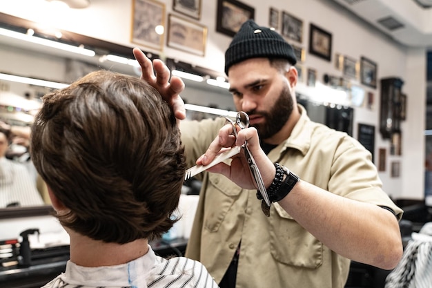 Friseur hackt Haare des braunhaarigen männlichen Modells. Prozess der Erstellung einer neuen Frisur.