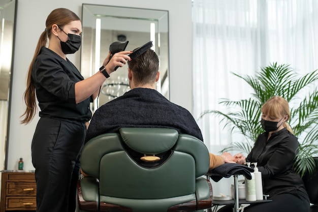 Friseur in Schutzmaske, der dem Kunden Haare trocknet