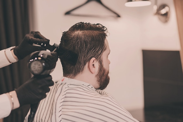 Friseur in schwarzen Handschuhen trocknet den Kopf eines Mannes