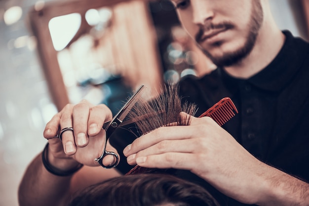 Friseur kämmt hübsches Mannhaar mit Händen.