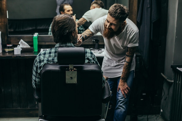 Friseur lächelte freundlich, während er sich an seinen Klienten lehnte und seinen Bart kämmte