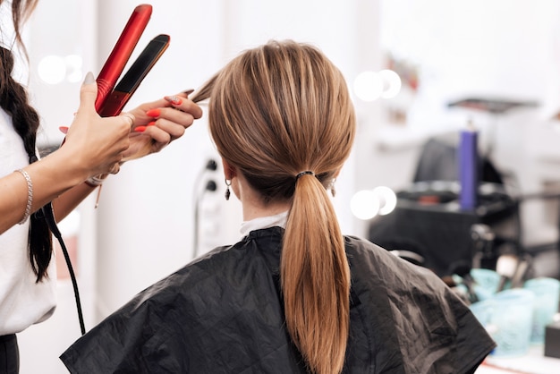 Friseur macht eine Frisur für eine Frau mit hellbraunen langen Haaren