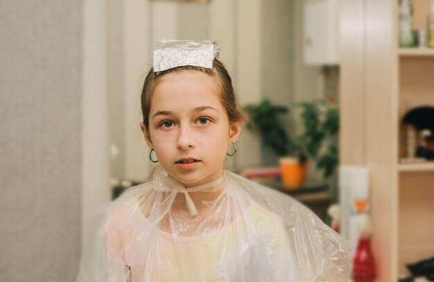 Friseur macht eine Frisur zu niedlichen kleinen Mädchen. Ein junges Mädchen hat ihren Pony in einem Schönheitssalon aufgehellt. Orange Pony. Der Trend zu hellem Haar.