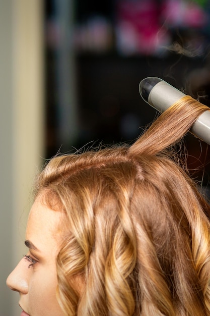 Friseur macht Locken mit einem Lockenstab für die junge Frau mit langen braunen Haaren in einem Schönheitssalon.