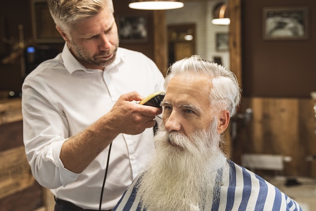 Friseur macht stilvollen Haarschnitt für einen gutaussehenden alten Mann im Friseursalon