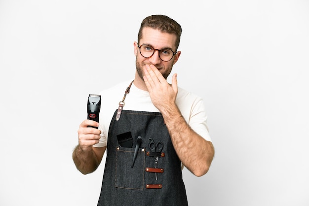 Friseur Mann in einer Schürze über isoliertem weißem Hintergrund glücklich und lächelnd den Mund mit der Hand bedeckend