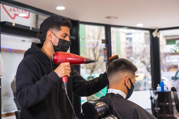 Friseur mit Gesichtsmaske, die den Schnitt zum Kunden fertigstellt