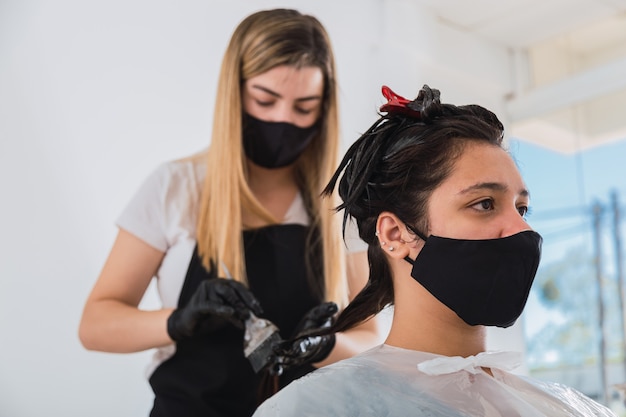 Friseur mit Gesichtsmaske und Handschuhen, die Farbstoff auf den Kunden auftragen