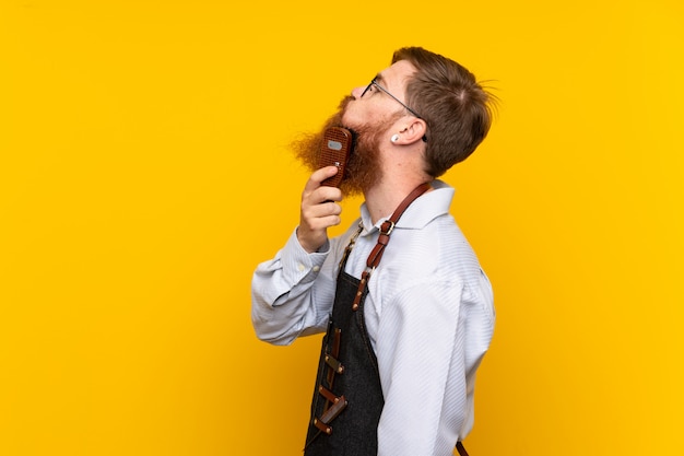 Friseur mit langem Bart in einem Schutzblech über getrenntem gelbem Hintergrund