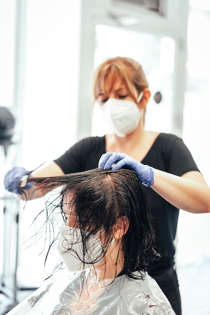 Friseur mit Maske und Handschuhen kämmen den Kunden. Wiedereröffnung mit Sicherheitsmaßnahmen von Friseuren in der Covid-19-Pandemie