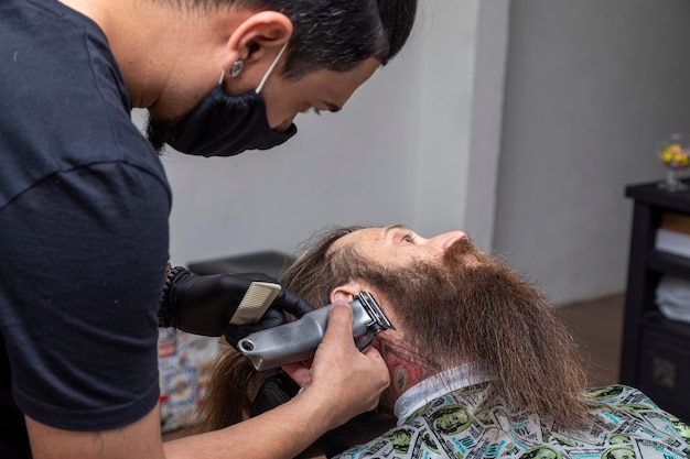 Friseur mit Rasierer, um den Bart eines Mannes zu schneiden.