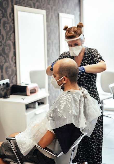 Friseur mit Sicherheitsmaßnahmen für den Covid-19, neue Normalität, soziale Distanz, Friseur und Kunde mit Maske. Kurze kurze Haare schneiden