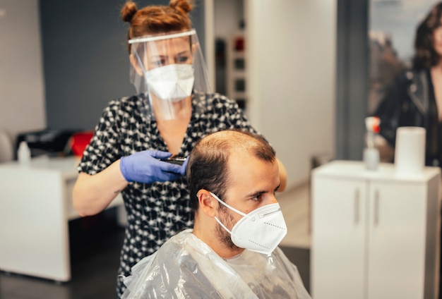 Friseur mit Sicherheitsmaßnahmen für die Covid-19, neue Normalität, soziale Distanz, Haare schneiden mit einer Maske