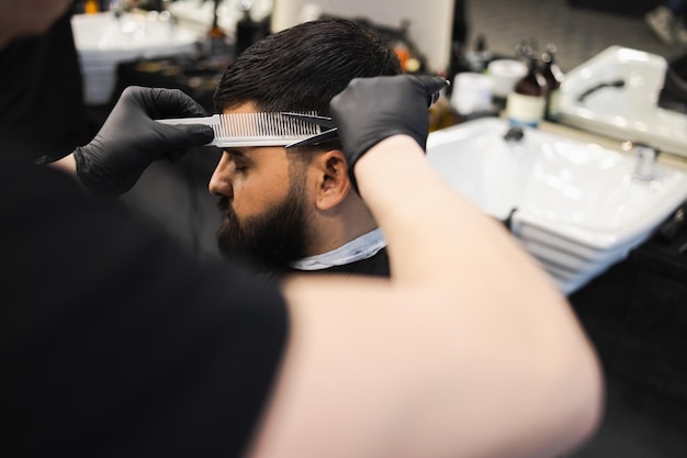 Friseur schert Haare an den Kopfseiten für einen stilvollen schwarzhaarigen Mann im Friseursalon