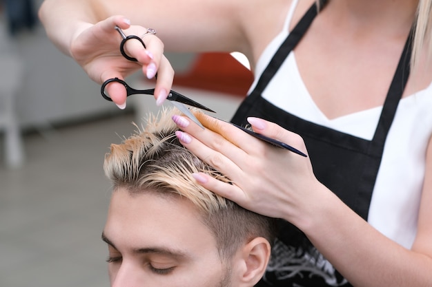 Friseur schneidet einem jungen Mann mit blond gefärbten Haaren mit einer Schere in einem Schönheitssalon die Haare. Professionelle Haarpflege.