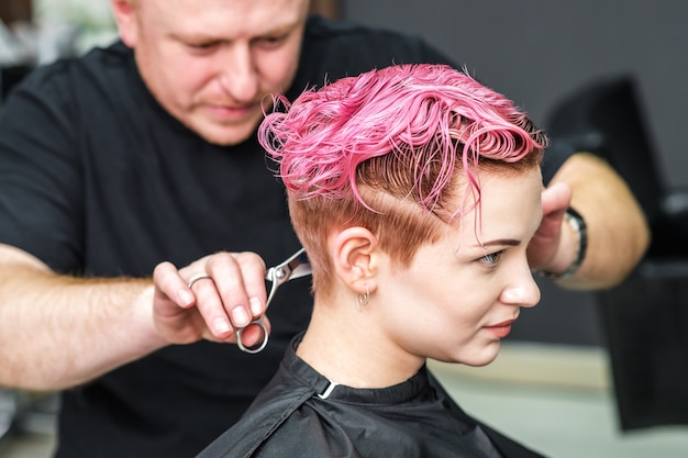Friseur schneidet rosa Haare einer Frau.