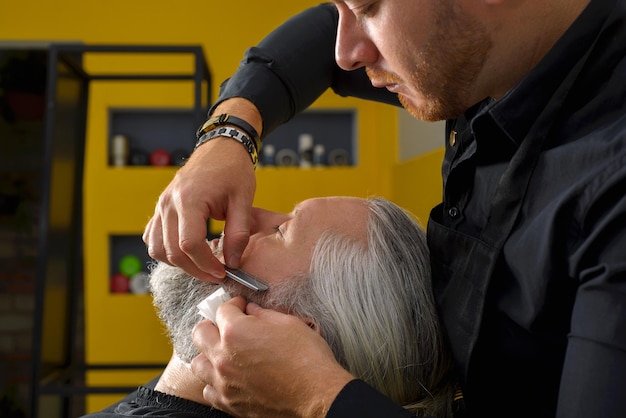 Friseur schneidet und stylt den Bart eines grauhaarigen Mannes. Bartschneide- und Stylingprozess