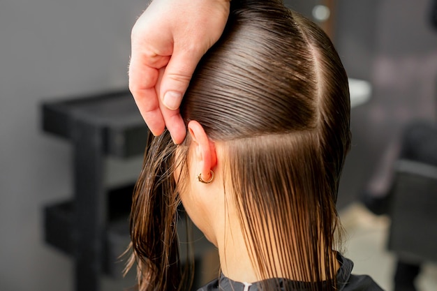 Friseur teilt weibliches Haar in Abschnitte mit Kamm, der das Haar mit den Händen im Friseursalon hält.