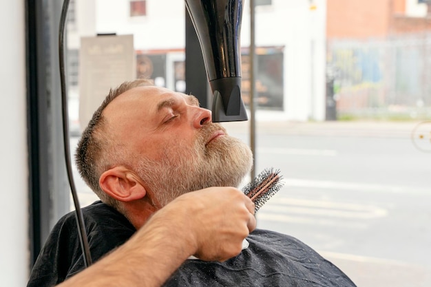 Friseur trimmt und schneidet bärtigen Mann mit Rasiermaschine im Friseursalon Hairstyling-Prozess