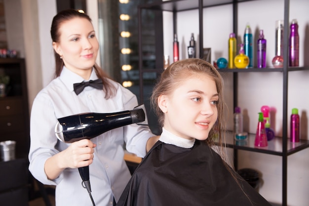 Friseur trocknet blondes Haar mit Fön im Salon