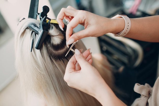 Friseurfrau, die junge Frau mit blonden Haaren im Schönheitssalon Haarverlängerungen macht. Professionelle Haarverlängerung.