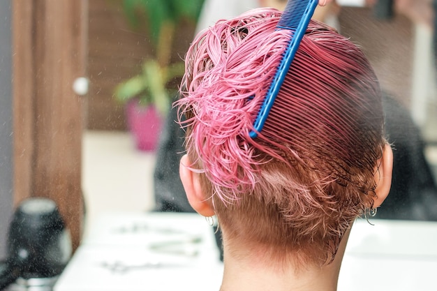 Friseurhände sprühen Wasser auf rosa Haare der Frau im Friseursalon.