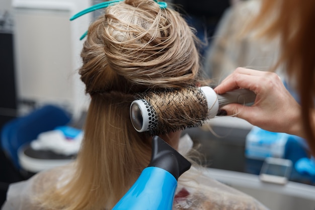 Friseurhände trocknen blondes Haar mit Föhn und Rundbürste