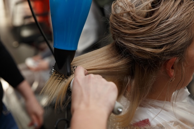 Friseurhände trocknen blondes haar mit föhn und rundbürste