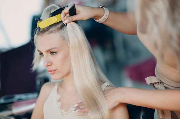 Friseurin, die Haarverlängerungen zu junger Frau mit blondem Haar im Schönheitssalon professionelle Haarverlängerung macht