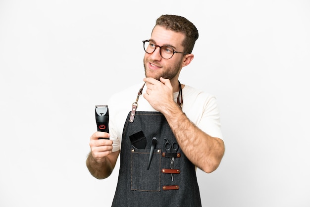 Friseurmann in einer Schürze über isoliertem weißem Hintergrund, der zur Seite schaut und lächelt