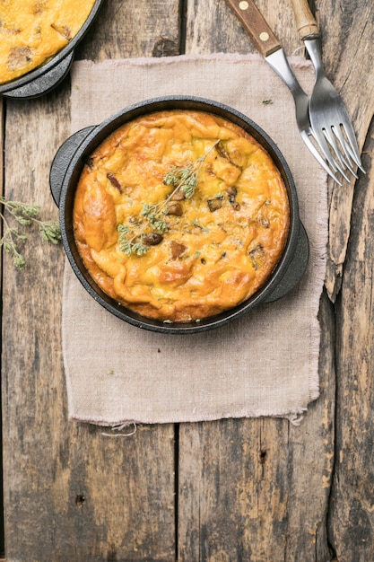 Fritada com cogumelos em uma panela com fundo de madeira. Fritata é um prato italiano de café da manhã.