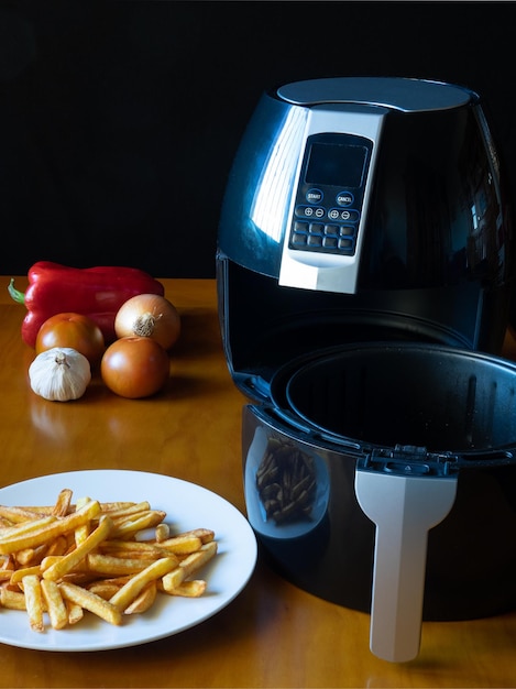 Fritadeira ao ar livre com cesta em uma mesa com batatas fritas e legumes Conceito de comida saudável