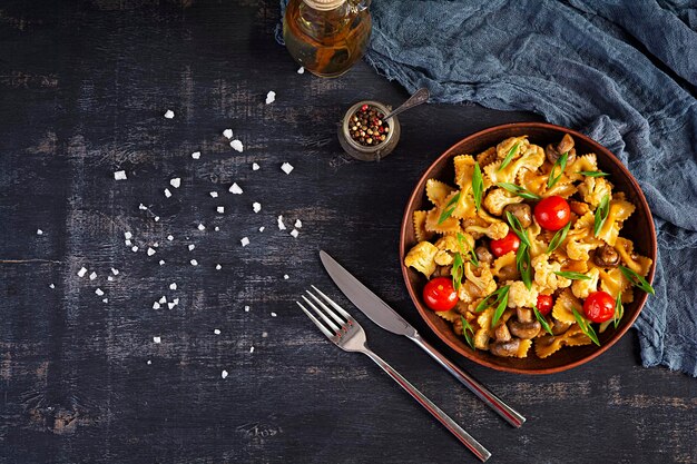 Foto fritar farfalle pasta com legumes couve-flor e cogumelos vista superior