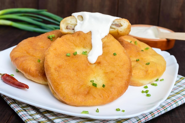 Fritar tortas com carne em um prato branco com creme azedo no fundo escuro de madeira