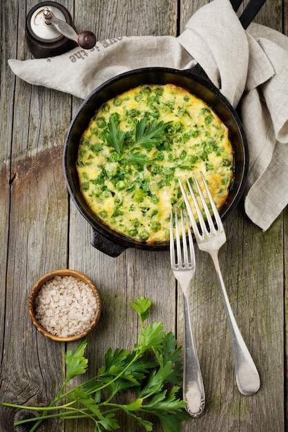 Fritatta con patatas, guisantes y hierbas en una sartén de hierro sobre una superficie de madera vieja