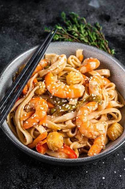 Frite macarrão udon de frutos do mar com camarões em uma tigela. Fundo preto. Vista do topo.