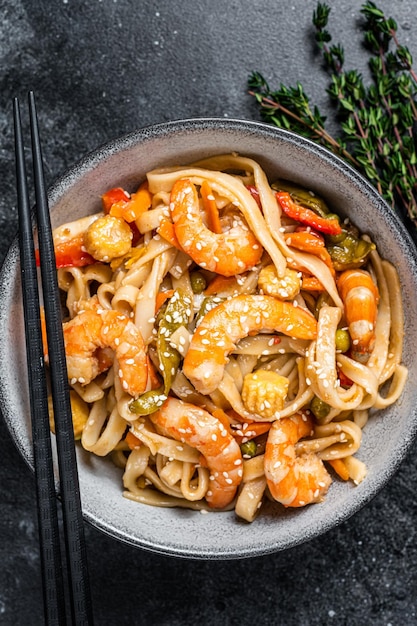 Frite macarrão udon de frutos do mar com camarões em uma tigela. Fundo preto. Vista do topo.