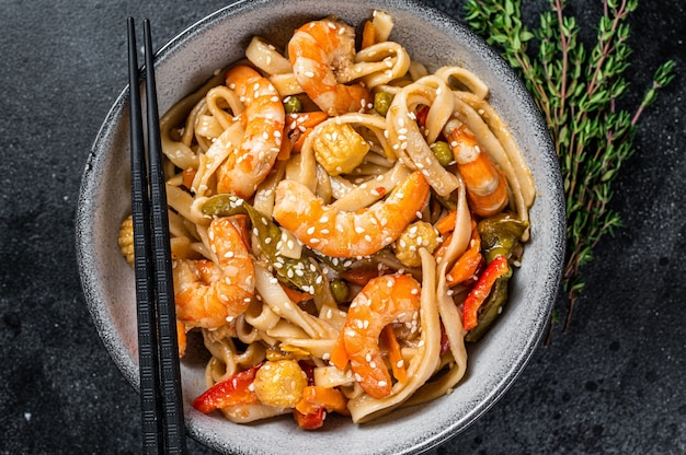 Frite macarrão udon de frutos do mar com camarões em uma tigela. Preto