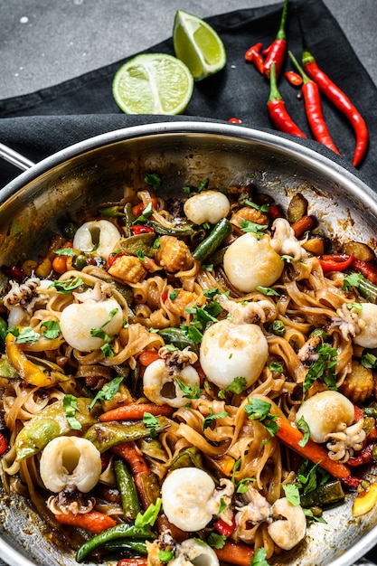 Frite o macarrão com frutos do mar e legumes em uma panela wok. fundo preto. vista do topo