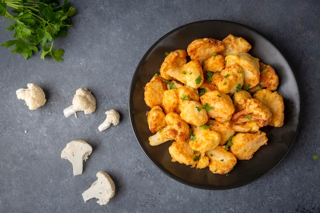 Frito em massa Floretes de couve-flor servidos em um prato preto em uma mesa de concreto cinza com ingredientes vista de cima do espaço de cópia flatlay closeup