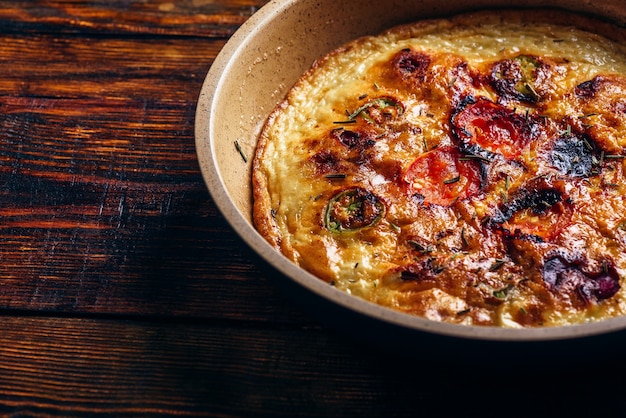 Frittata cocida con chorizo, tomates y chiles en una sartén sobre fondo de madera oscura. Vista de ángulo alto.