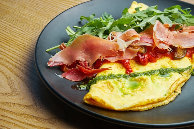 Frittata con jamón serrano, salsa de pesto, rúcula y pimiento en plato negro. Almuerzo sabroso y saludable. Tortilla