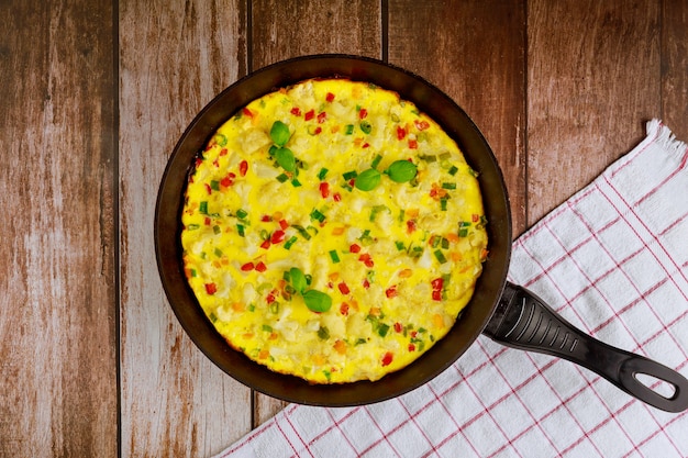 Frittata mit käse, blumenkohl, grünem und rotem paprika in eisenpfanne.